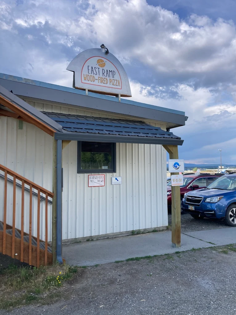 The East Ramp Wood-Fired Pizza building — a white metal shed with a pizza-shaped sign and stairs up the side