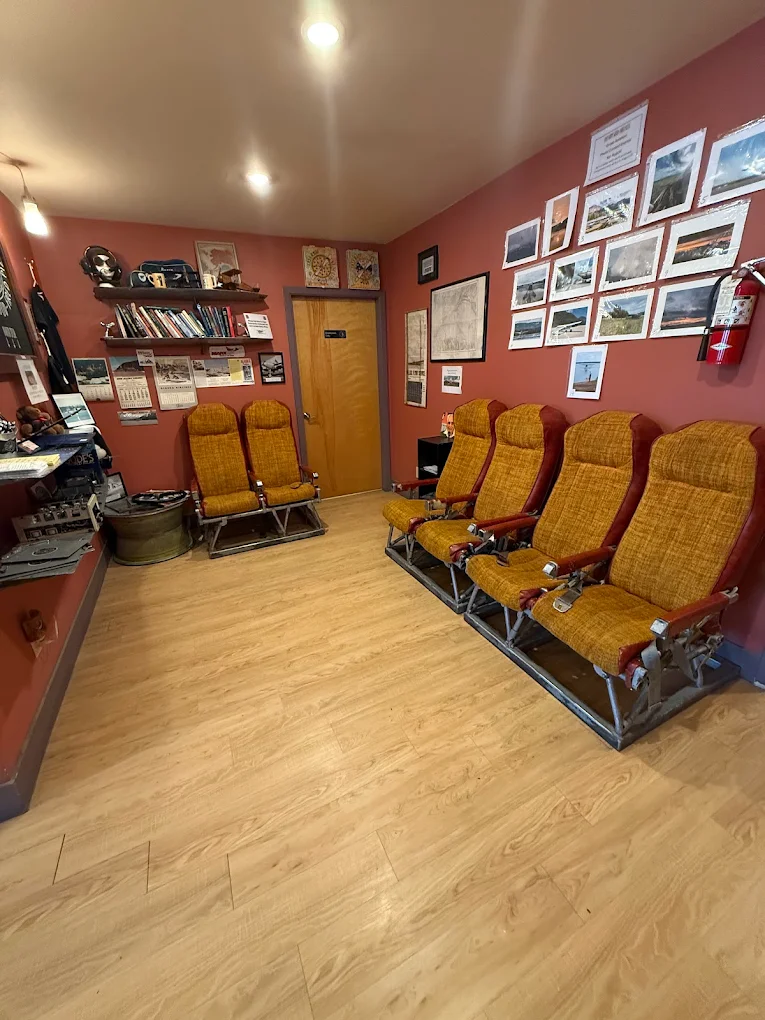 Vintage upholstered airplane seats arranged in the East Ramp waiting room, with dusty-rose walls covered in framed Alaska aviation photography